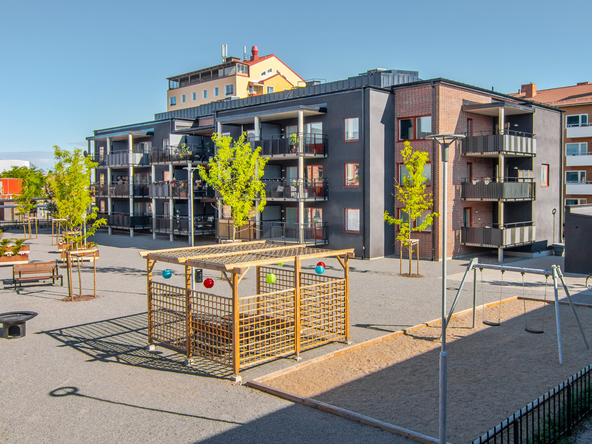 Innegård med pergola, fastighet med tre våningar i bakgrunden.