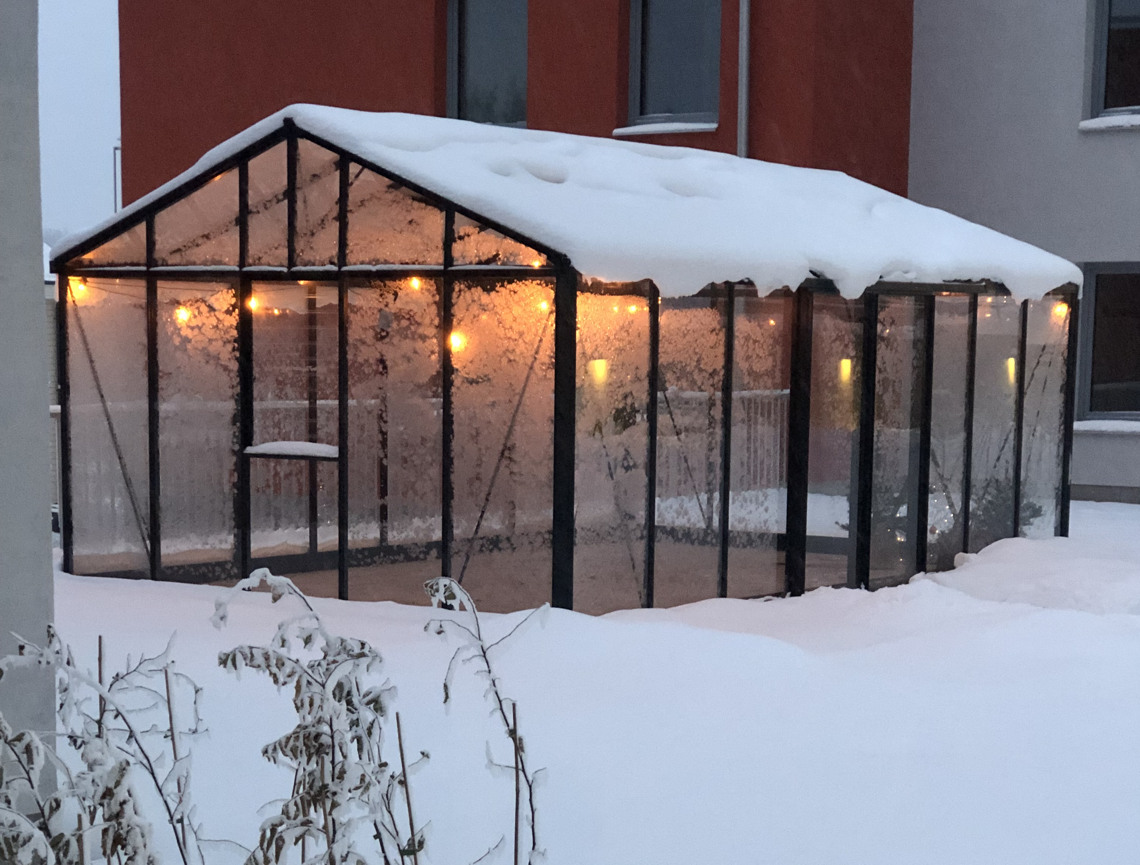 Snötäckt, frostigt växthus med belysning inuti. Utanför ligger snö.
