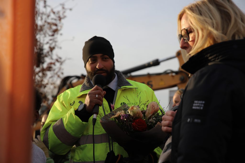 Bild på byggprojektledare som håller i mikrofon och blombukett. 